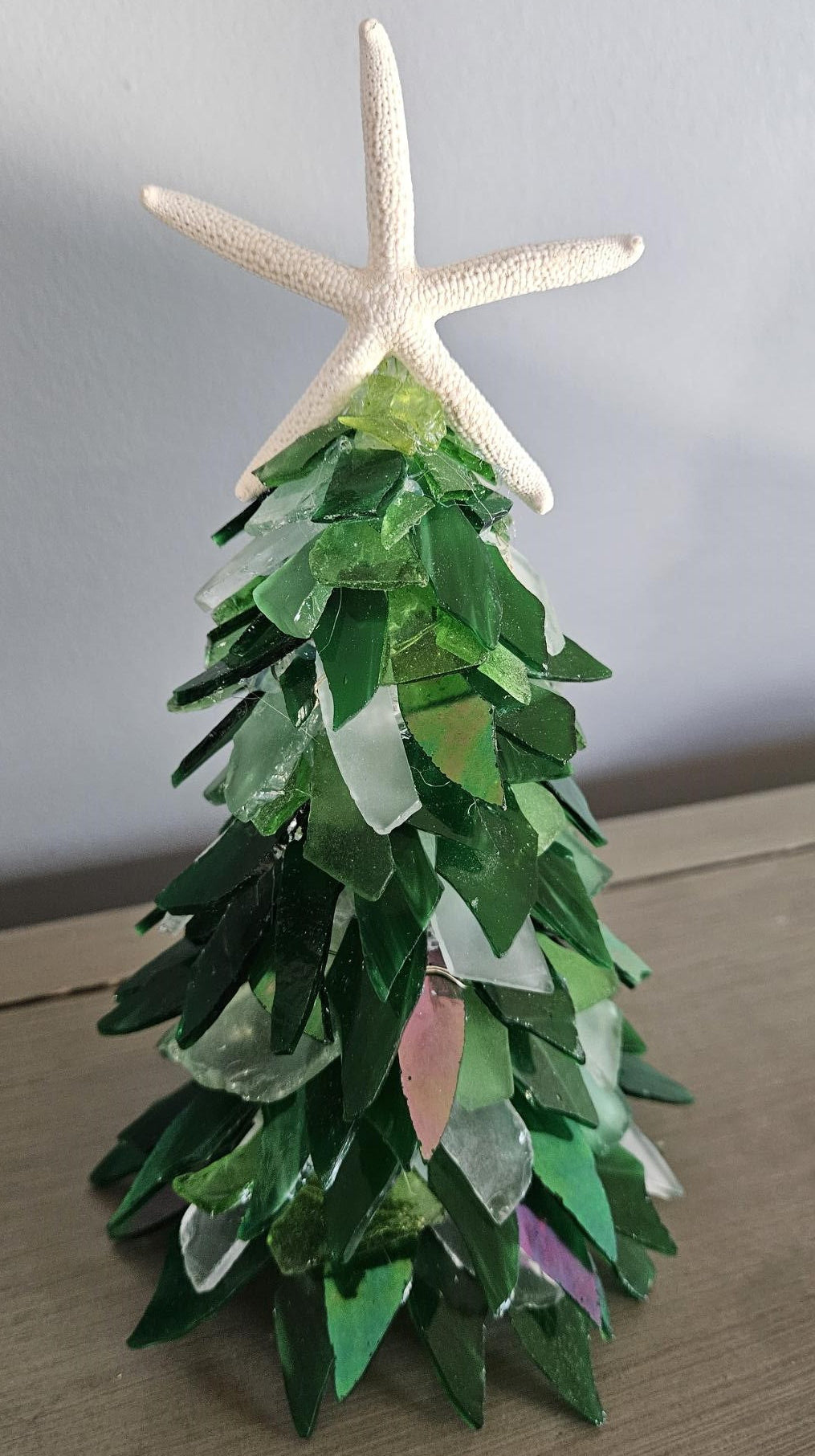 Decorative Christmas tree made of green glass with a starfish on top against a plain background