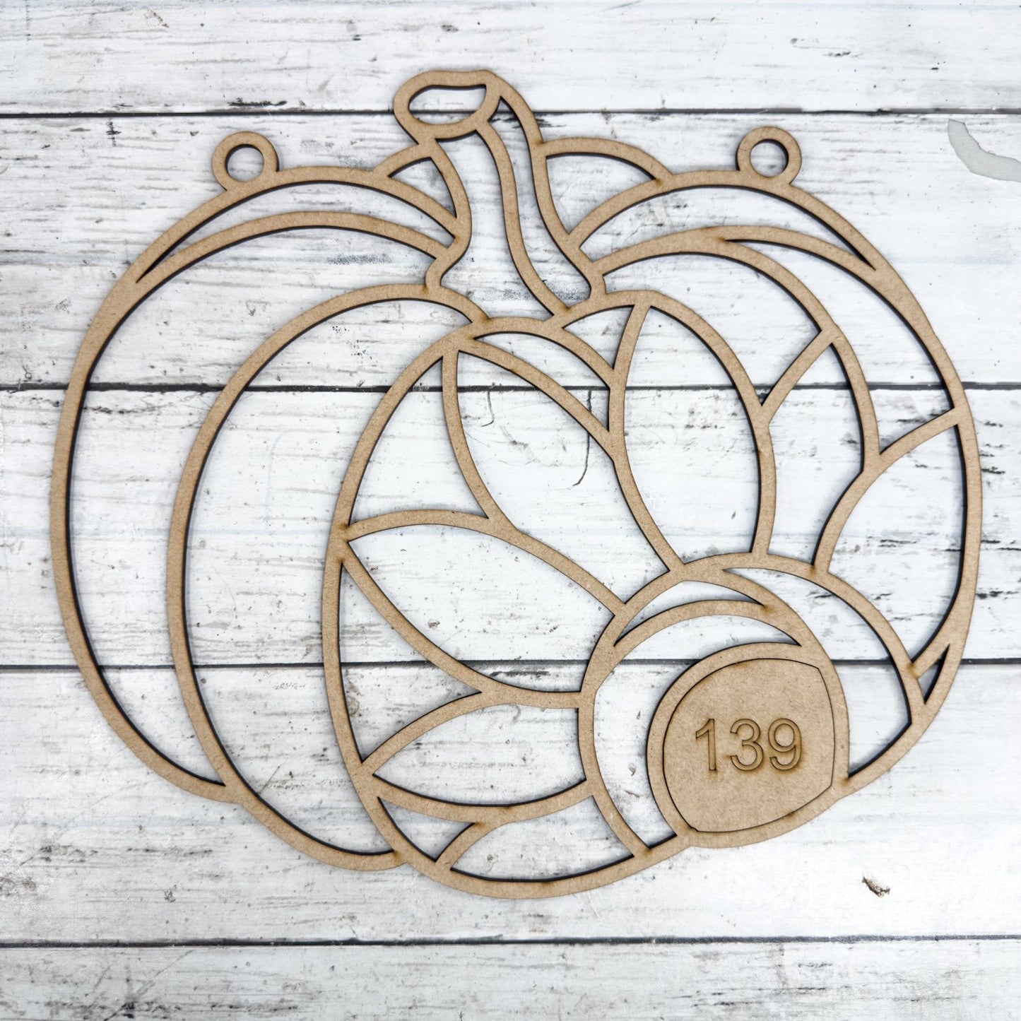 Wooden pumpkin-shaped cutout with the number 139 on a white wooden surface