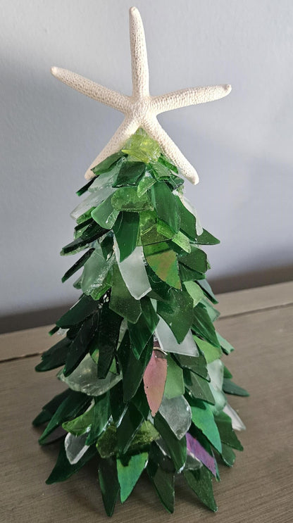 Decorative Christmas tree made of green glass with a starfish on top against a plain background