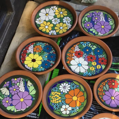 Collection of mosaic flower and bee designs on small round terracotta plates.