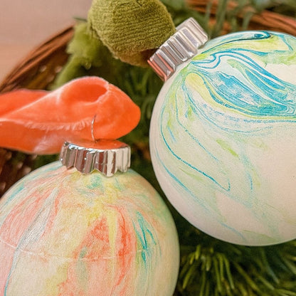 Two marbled Christmas ornaments with colorful swirl patterns on a green wreath.