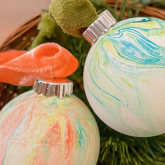 Two marbled Christmas ornaments with colorful swirl patterns on a green wreath.