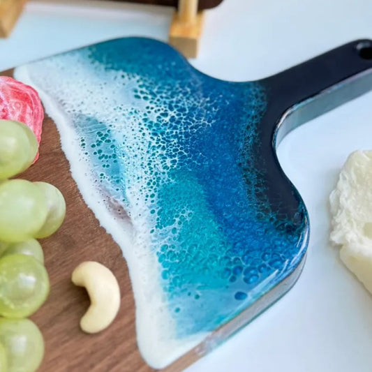 Blue and white ceramic dish with a wavy design on a wooden surface with fruits and cheese.