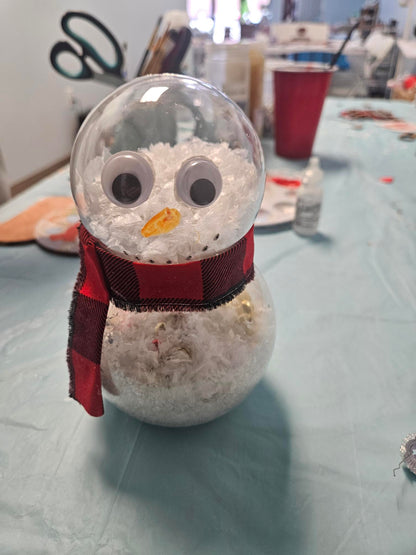Decorative snowman made from a spool of thread with googly eyes and a red ribbon on a light gray background.