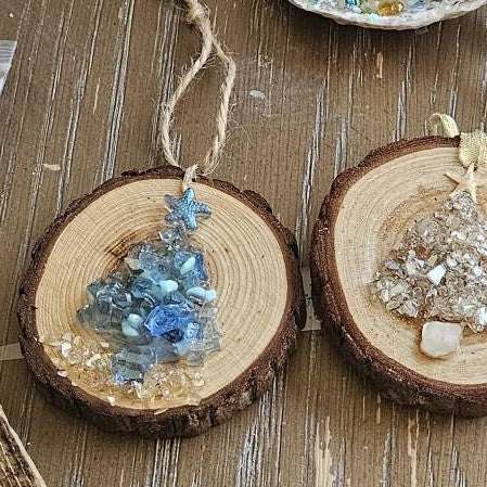 Two wooden Christmas tree ornaments with decorative crystals on a wooden surface.