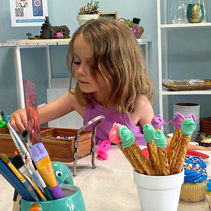 Child playing with art supplies and decorated pretzels in a casual indoor setting