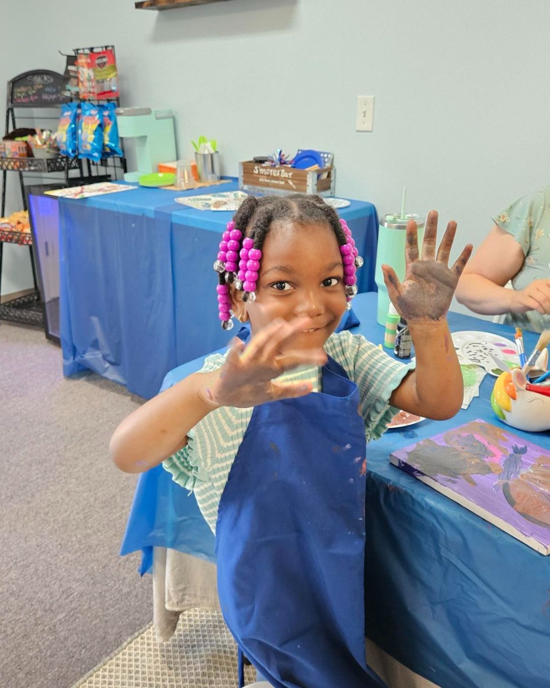 Child with paint on hands at a craft activity, wearing a blue apron.