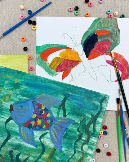 Colorful fish drawings on paper with art supplies around