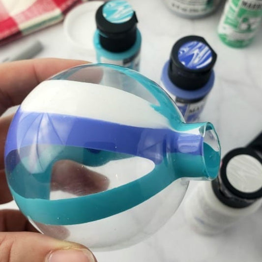 Clear plastic bottle with blue accents held by a hand, with ink bottles in the background.