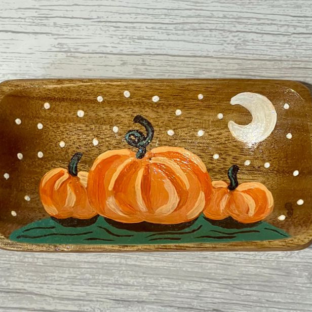 Wooden tray with painted pumpkins and a moon on a wooden surface